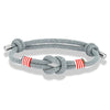 Bracelet nautique homme au cordage gris avec nœud marin central, surliures rouges doublées de blanc et embouts en acier poli